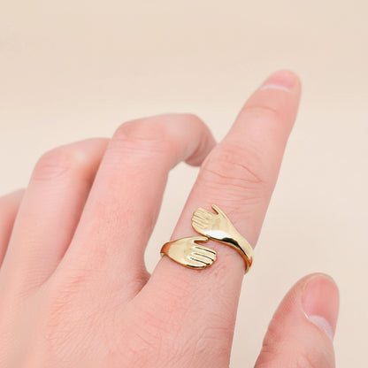 Gold hand-shaped ring on a finger against a white background