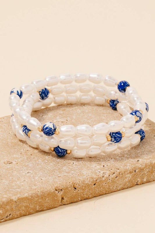 A white and blue beaded bracelet with floral patterns, displayed on a beige stone.