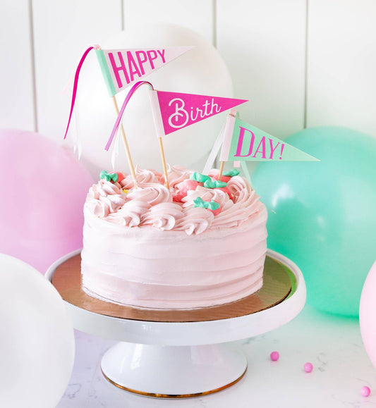 Pink birthday cake with decorative flags and balloons on a white background