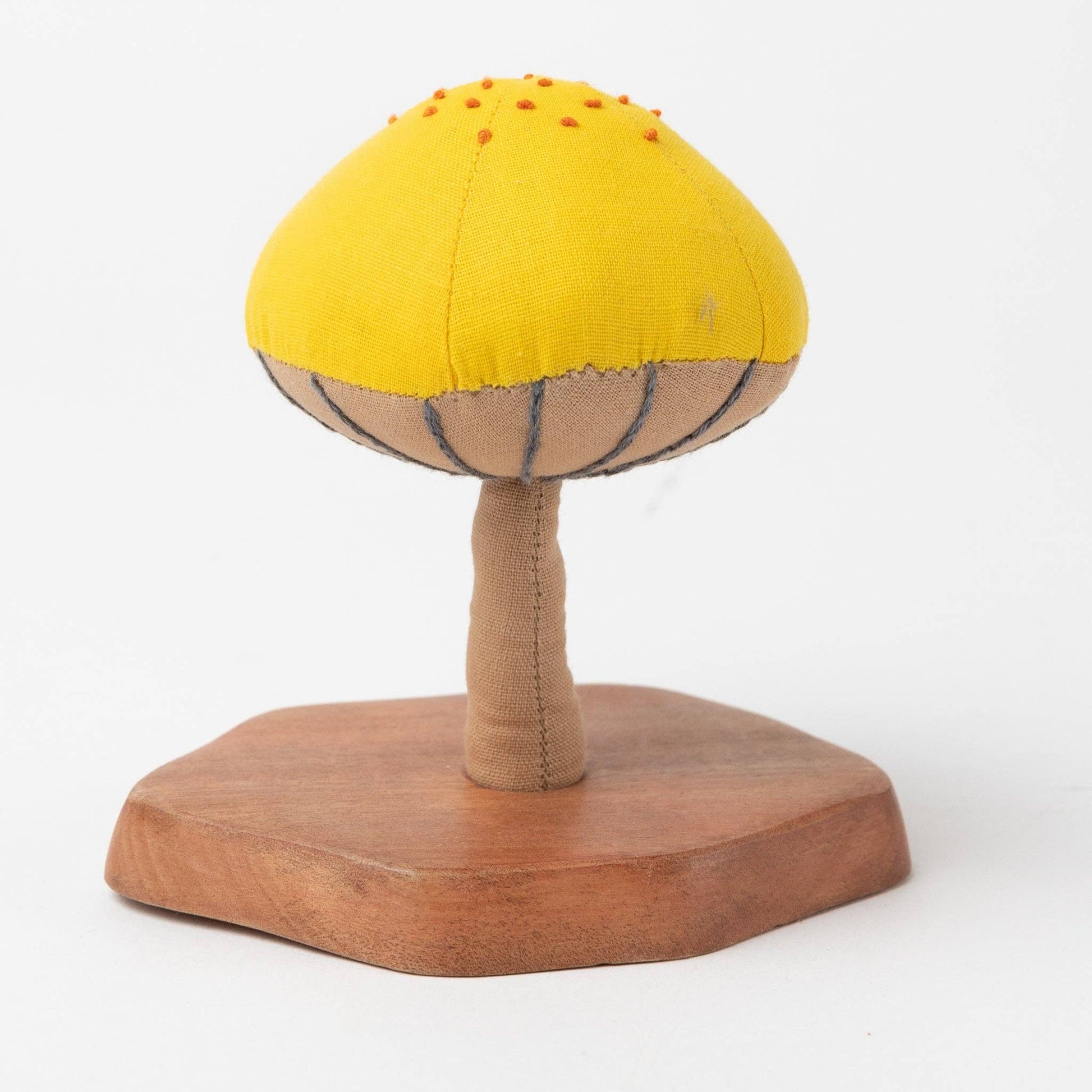 Single yellow and red mushroom sculpture on natural wood base