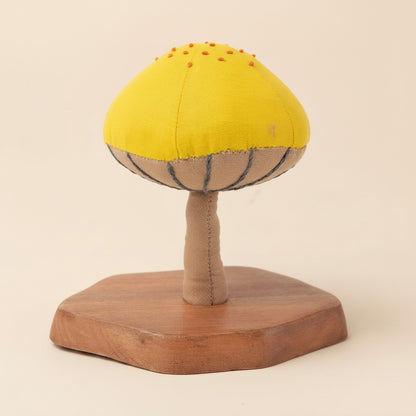 Single yellow and red mushroom sculpture on natural wood base