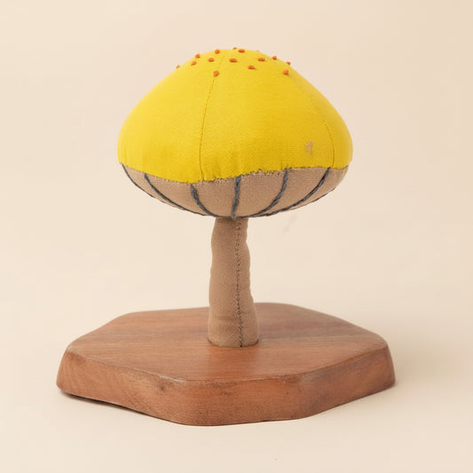 Single yellow and red mushroom sculpture on natural wood base