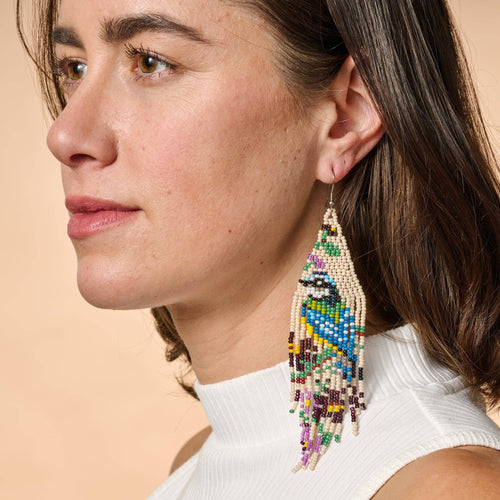 Close-up of a woman wearing colorful beaded earrings against a beige background