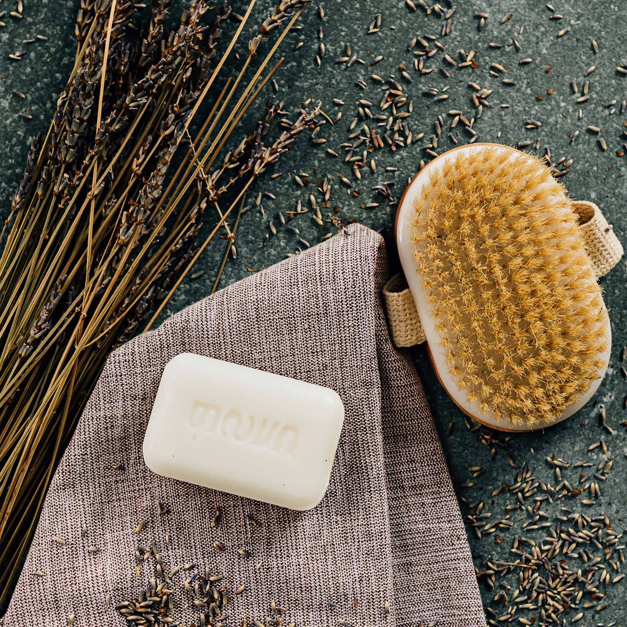 Bar of soap, natural brush, and lavender flowers on a textured surface