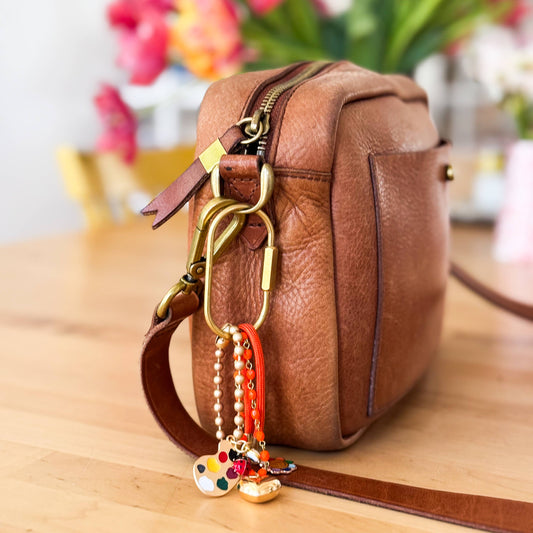 Rainbow-themed bag charm clipped to a vintage leather shoulder bag 
