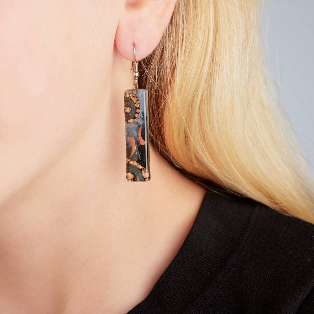 Close-up of artisan glass earrings showing unique swirls of color and enamel painting.