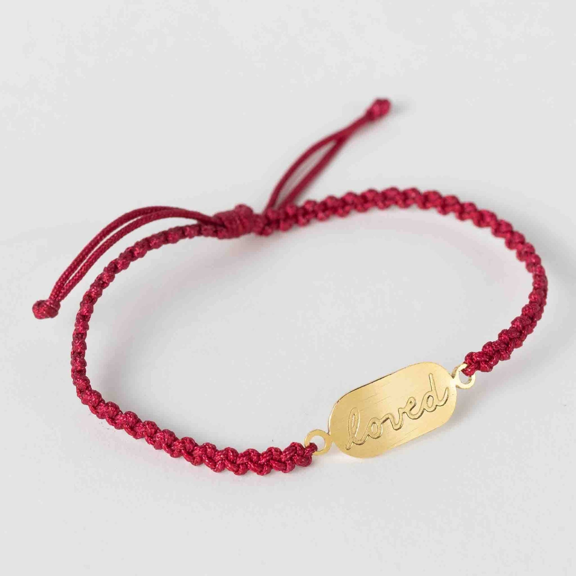 Red braided bracelet with a gold tag on a light gray background