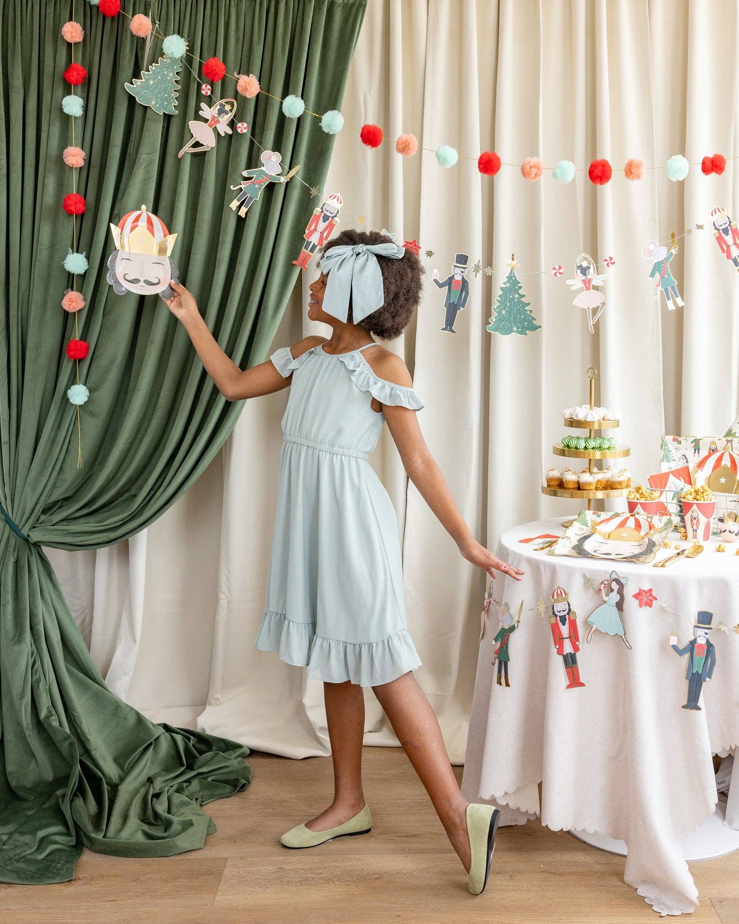 Child in a light blue dress standing next to a decorated table with a festive backdrop