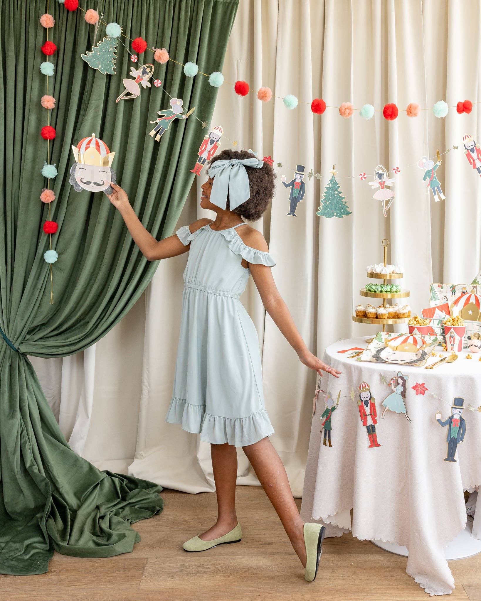 Child in a light blue dress standing next to a decorated table with a festive backdrop