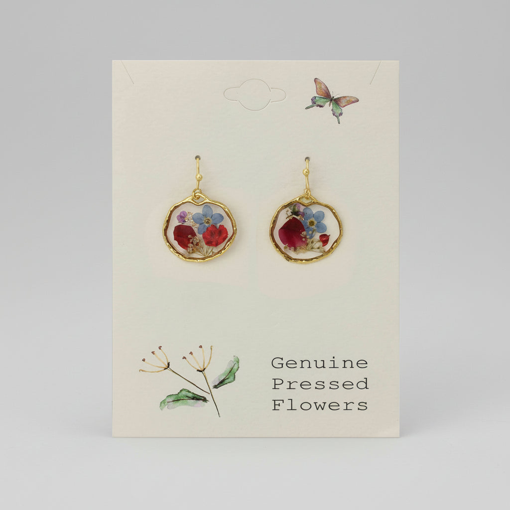 A pair of round floral earrings with blue and red dried flowers, encased in clear resin with a gold textured border, displayed on a card that reads 'Genuine Pressed Flowers'.