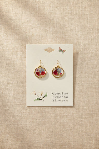 Gold earrings with floral designs on a card labeled 'Genuine Pressed Flowers' against a gray background