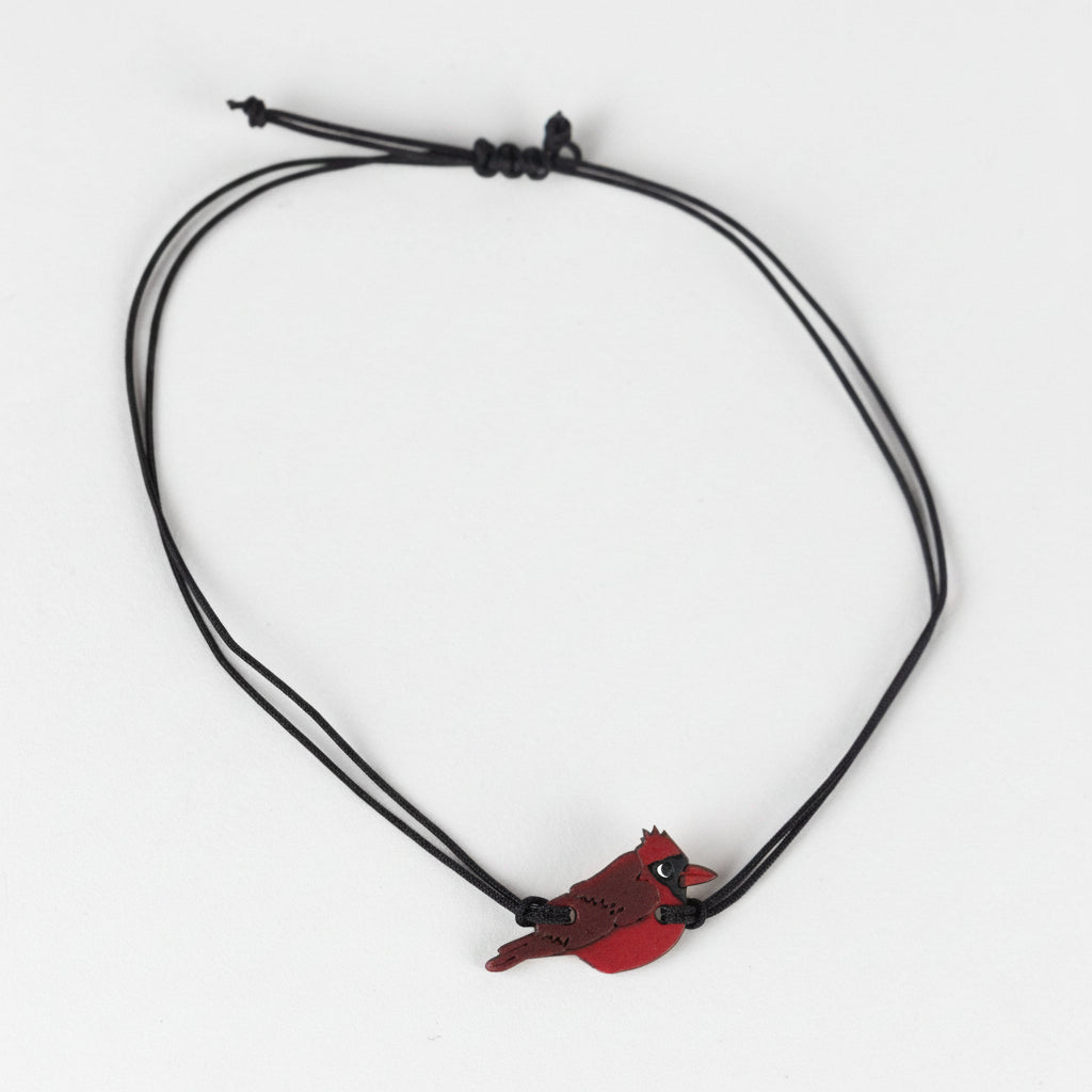 Bracelet with a Cardinal bird and black cords on a white background.