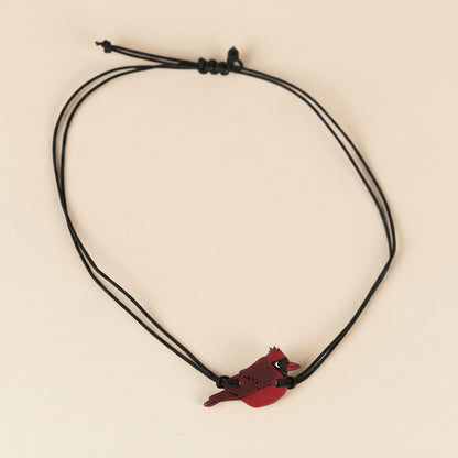 Bracelet with a Cardinal bird and black cords on a white background.