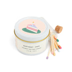 Birthday cake scented candle in white tin with corked vial of colorful matchsticks, packaged in a clear vinyl gift box.