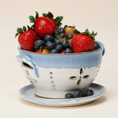 Ceramic colander filled with strawberries and blueberries on a white background