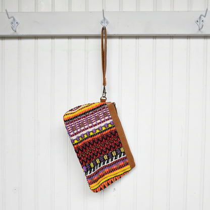 Colorful patterned pouch with a brown strap hanging on a white wooden panel.
