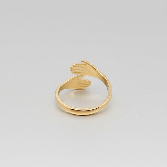 Gold ring shaped like a hand on a textured gray surface