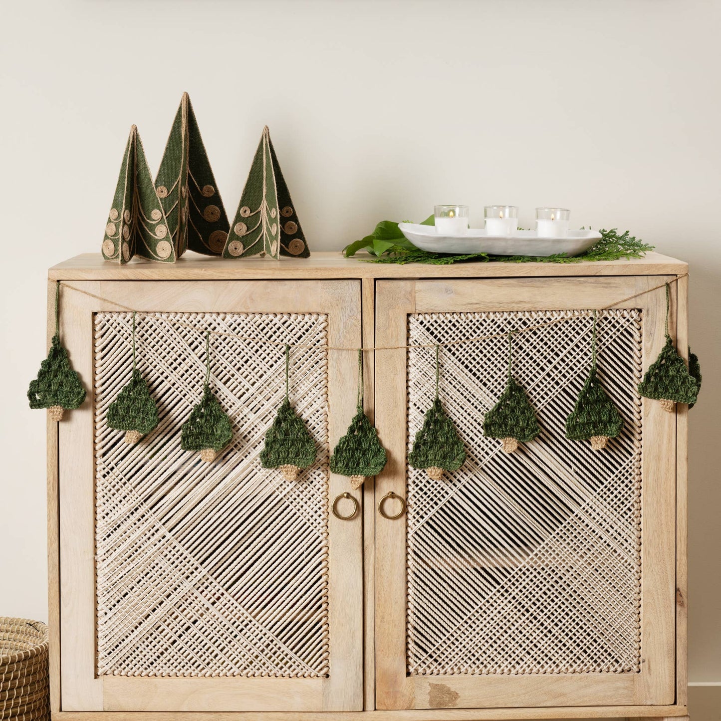 Holly Jolly Trees Crochet Garland draped across a buffet with other festive ornaments and decor with a neutral holiday background