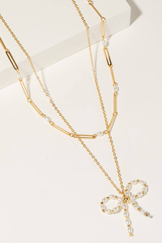 lose-up of pearl bow pendant layered on gold chains