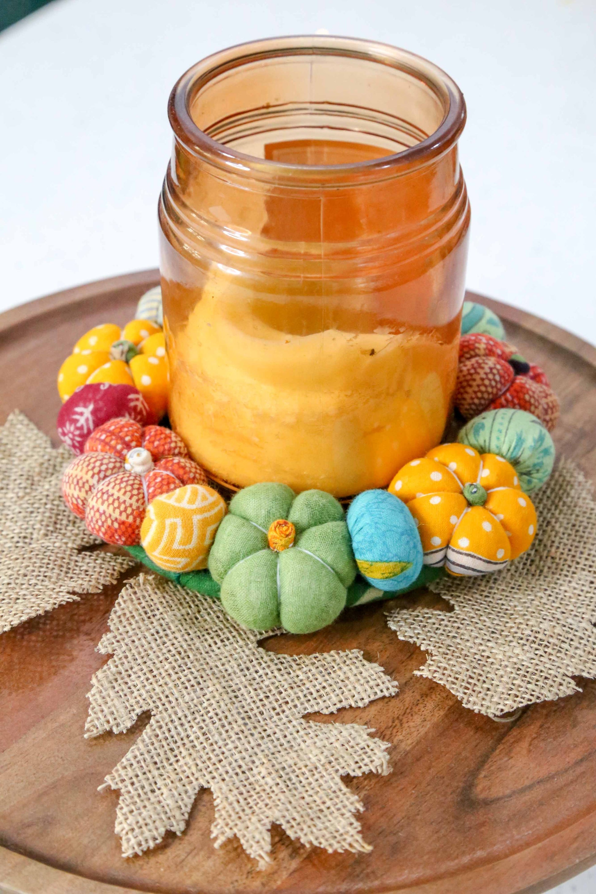 Candle in a glass jar with decorative pumpkins on a wooden surface
