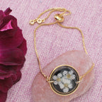 Gold necklace with a floral pendant on a pink textured background