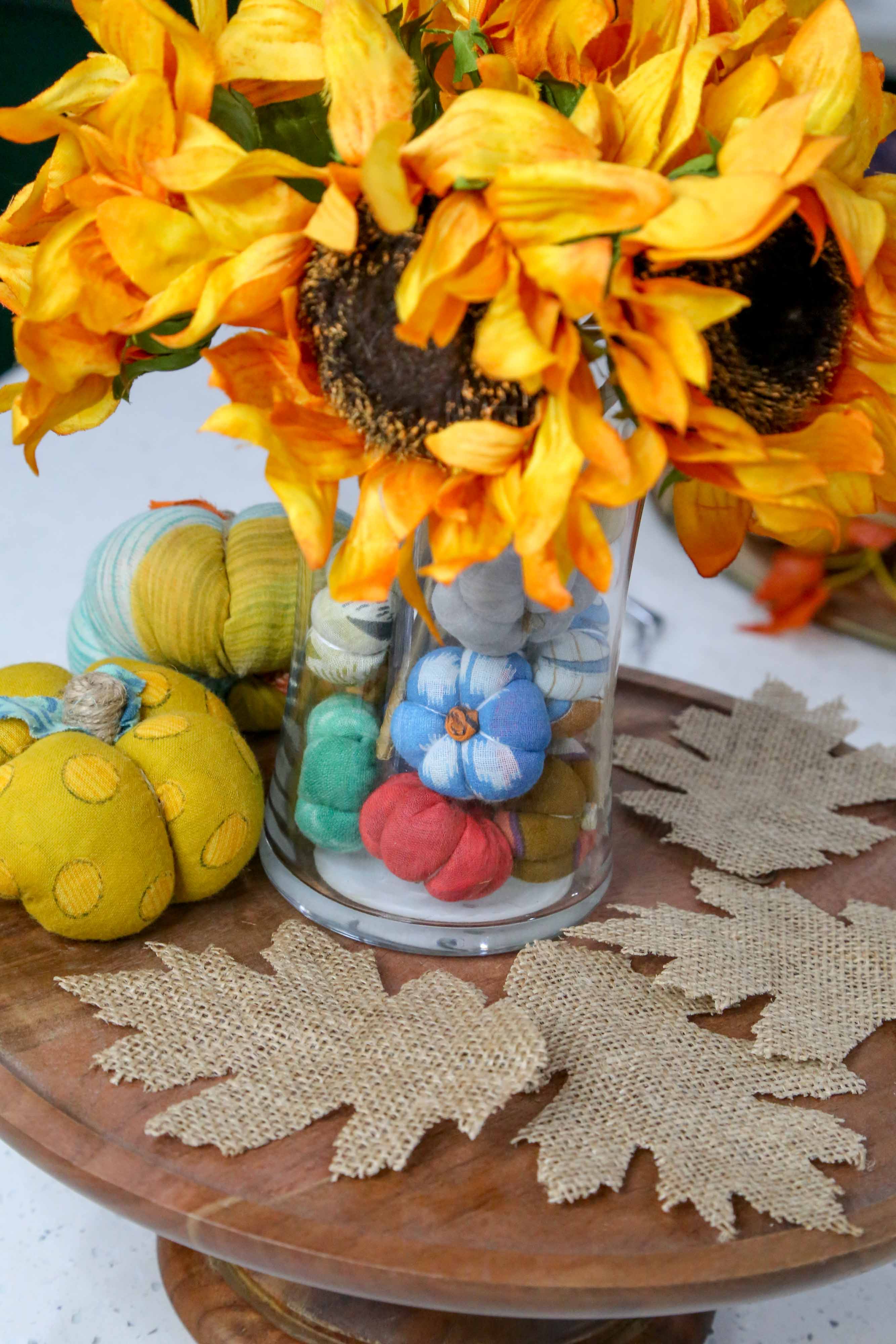 Sunflowers in a glass vase with decorative pumpkins and flowers on a wooden surface.