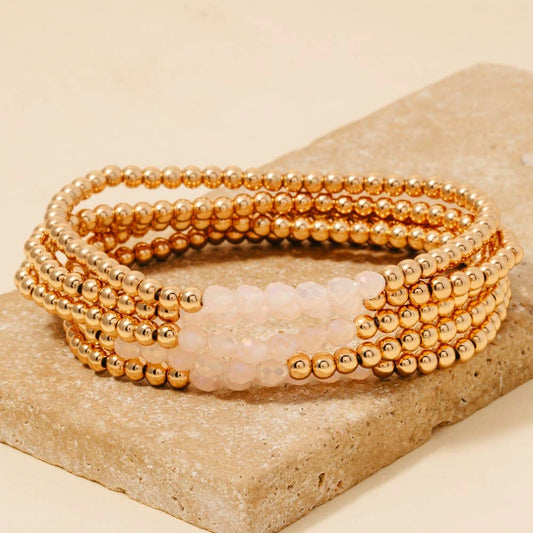 A set of gold metallic bead and pastel pink faceted glass bracelets displayed on a stone surface.
