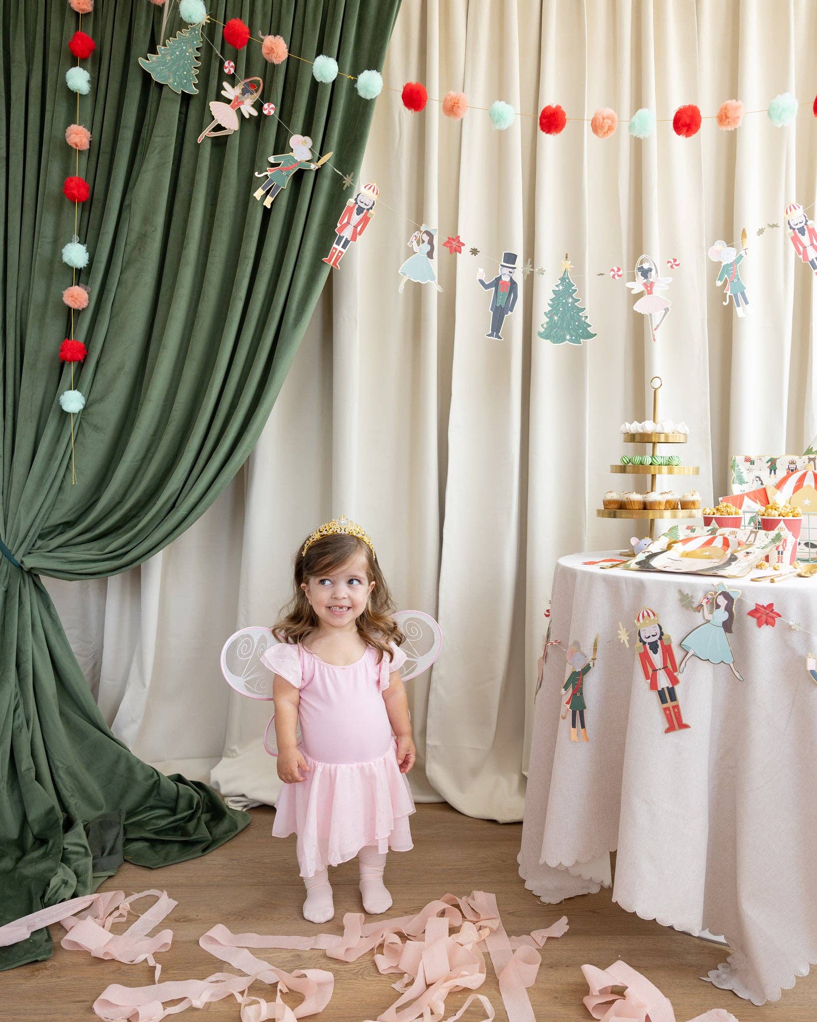 Child in fairy costume standing in a decorated room with green and white curtains and a table with treats.
