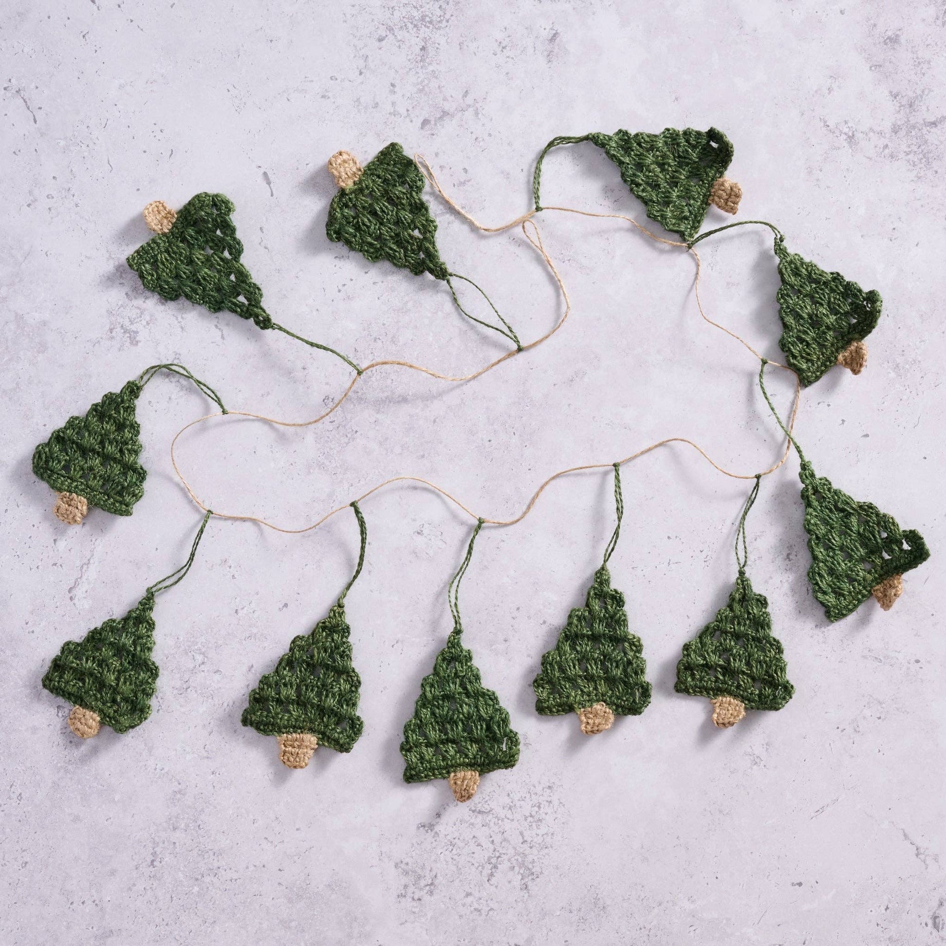 The Holly Jolly Trees Crochet Garland laid out on a marble countertop showcasing the length and amount of trees on each garland