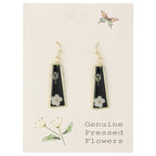 Black teardrop earrings with floral details on a beige card with botanical illustrations.