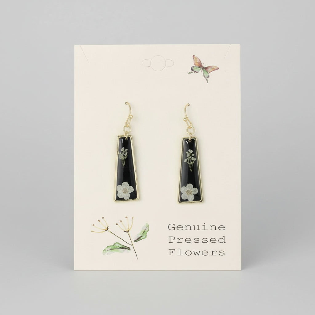Black teardrop earrings with floral details on a beige card with botanical illustrations.