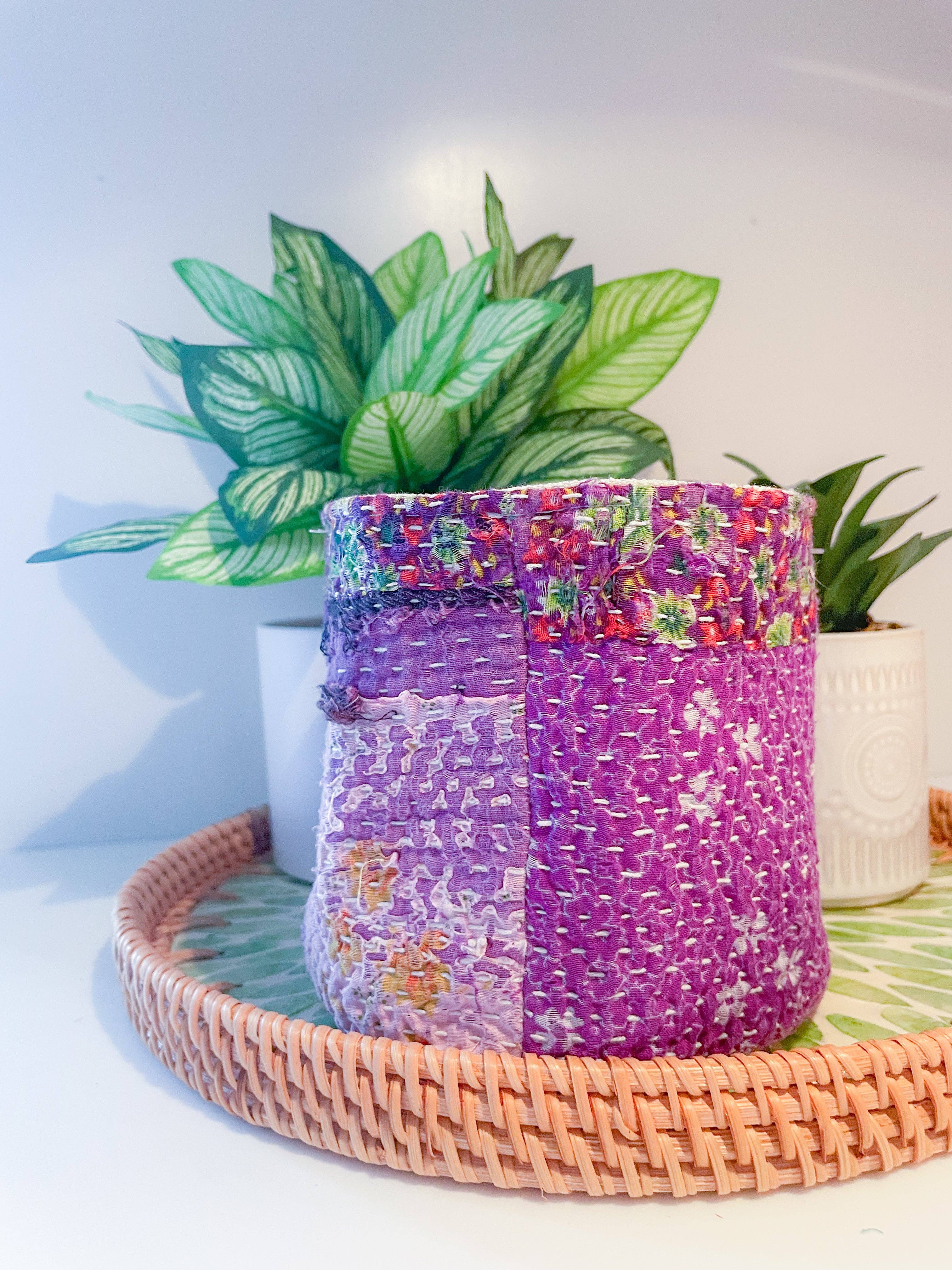 Decorative woven basket with floral patterns on a tray with plants in the background