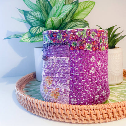 Decorative woven basket with floral patterns on a tray with plants in the background