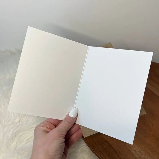 Close up image of a hand holding the white, blank interior of card against a neutral background