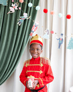 Child in a festive costume standing in front of decorated curtains with Christmas-themed decorations.