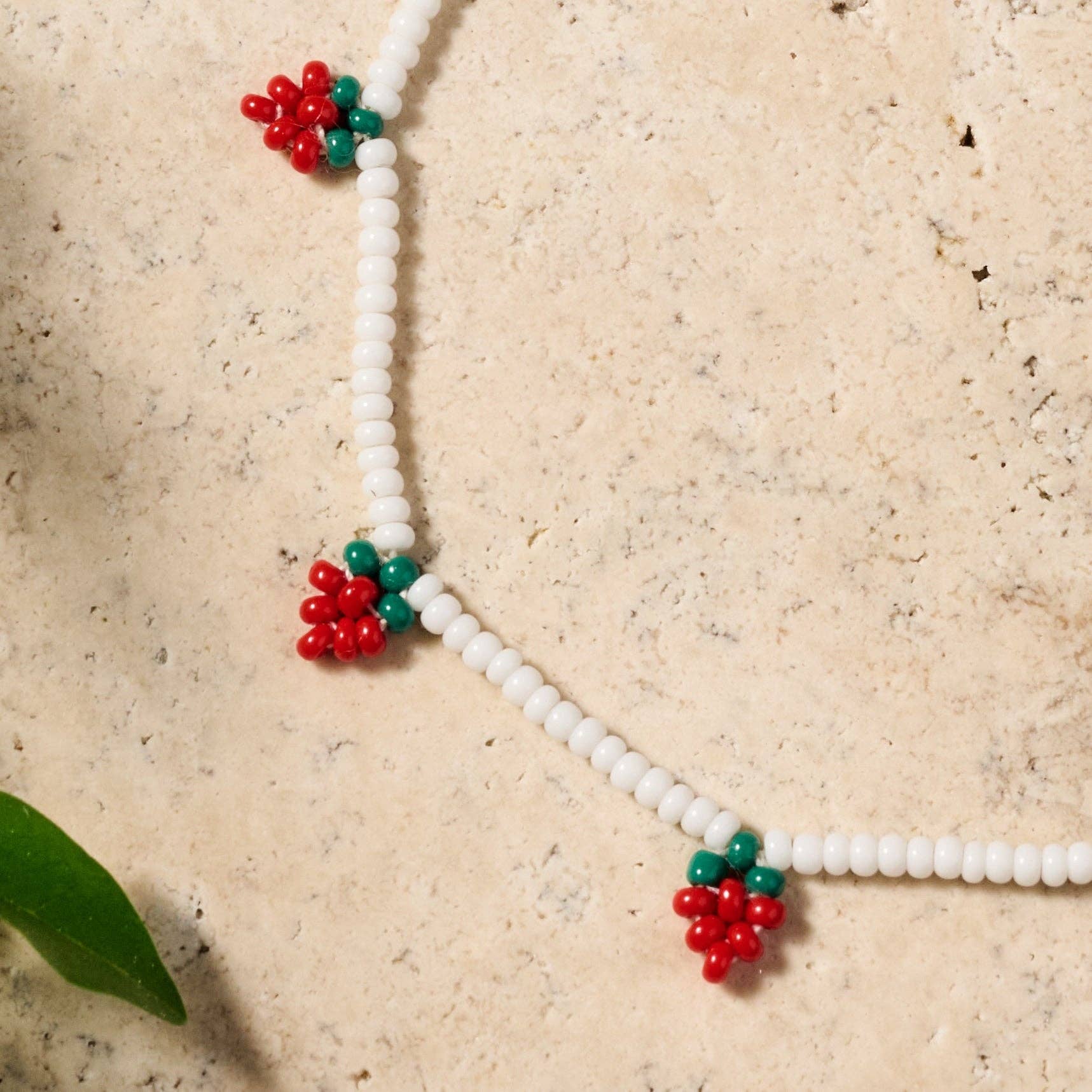 Close-up of delicate white glass bead bracelet featuring vibrant red and green strawberry beadwork