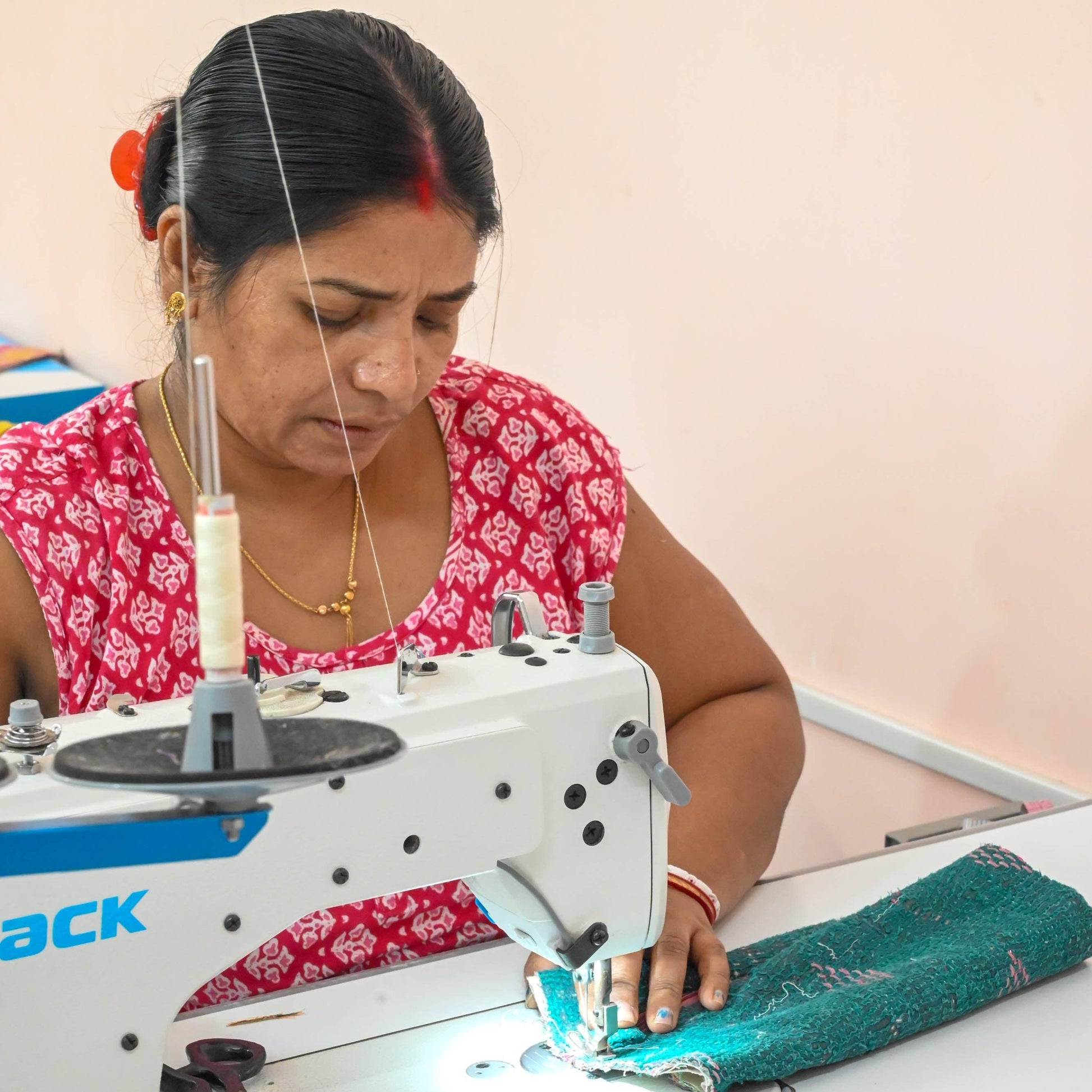 A woman from Asha Projects working on a sewing machine with a plain background
