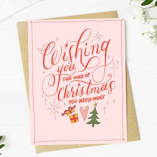 Pink Christmas card with red text and festive illustrations on a white background