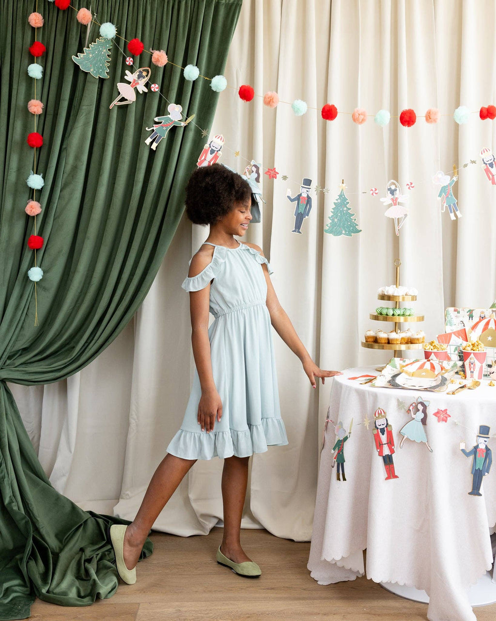 Young girl in a light blue dress standing next to a decorated table with festive decorations.