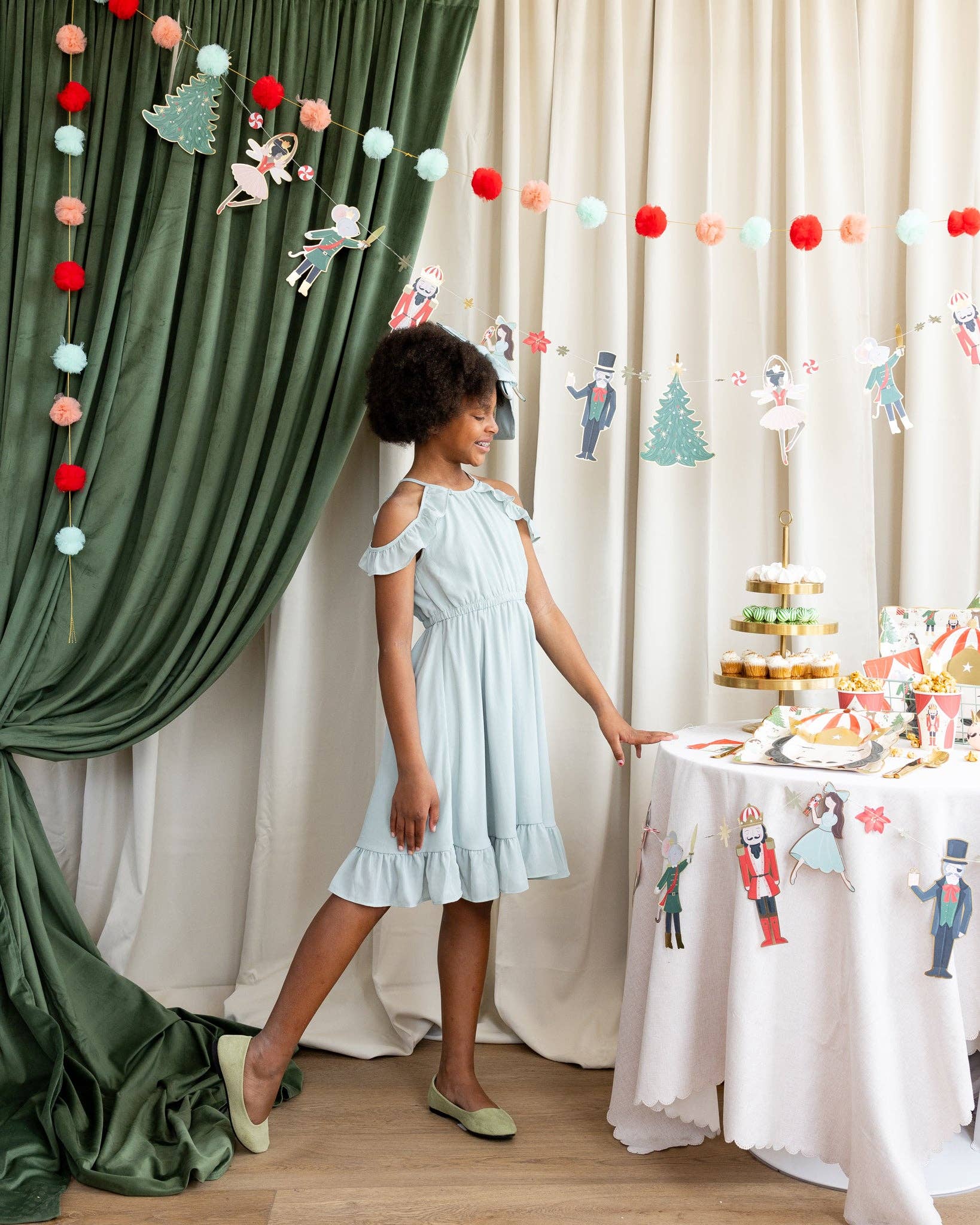 Young girl in a light blue dress standing next to a decorated table with festive decorations.