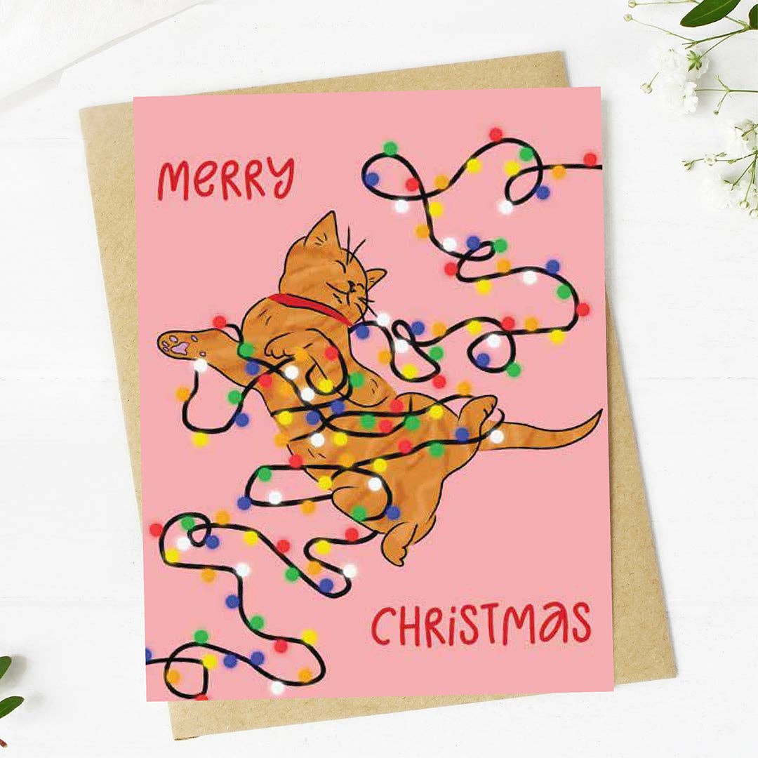 Pink holiday card with an orange playful cat, playing in color string lights with 'Merry Christmas' on the front