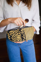 Person holding a black and gold patterned pouch with a makeup brush.