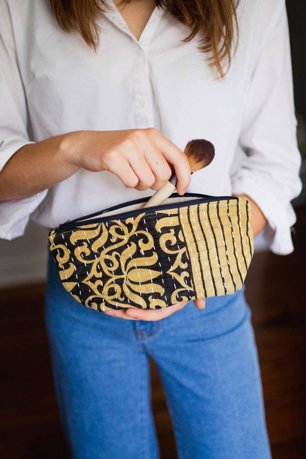 Person holding a black and gold patterned pouch with a makeup brush.