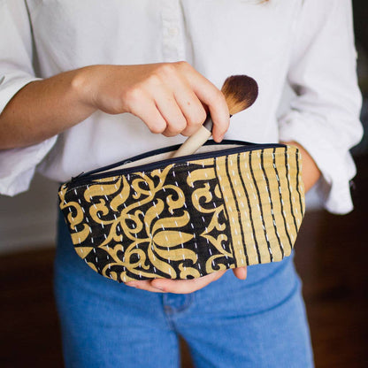 Person holding a black and gold patterned pouch with a makeup brush.