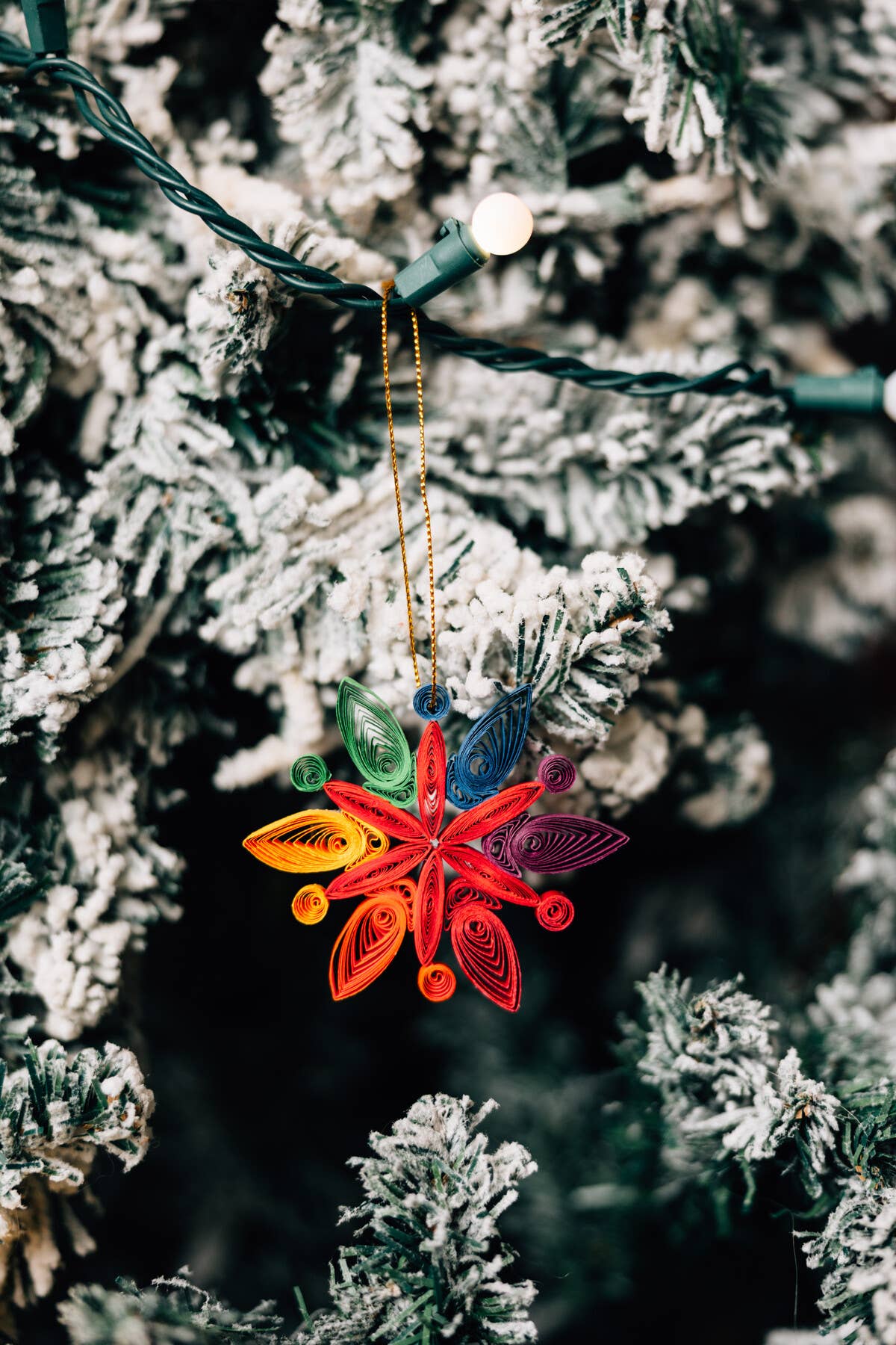 Colorful paper quilled ornament hanging on a frosted Christmas tree