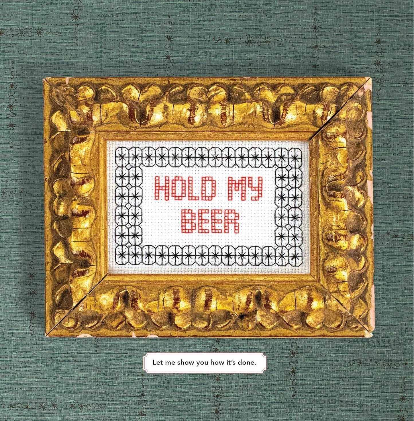 Gold-framed cross-stitched sign with 'Hold My Beer' text on a textured green background.