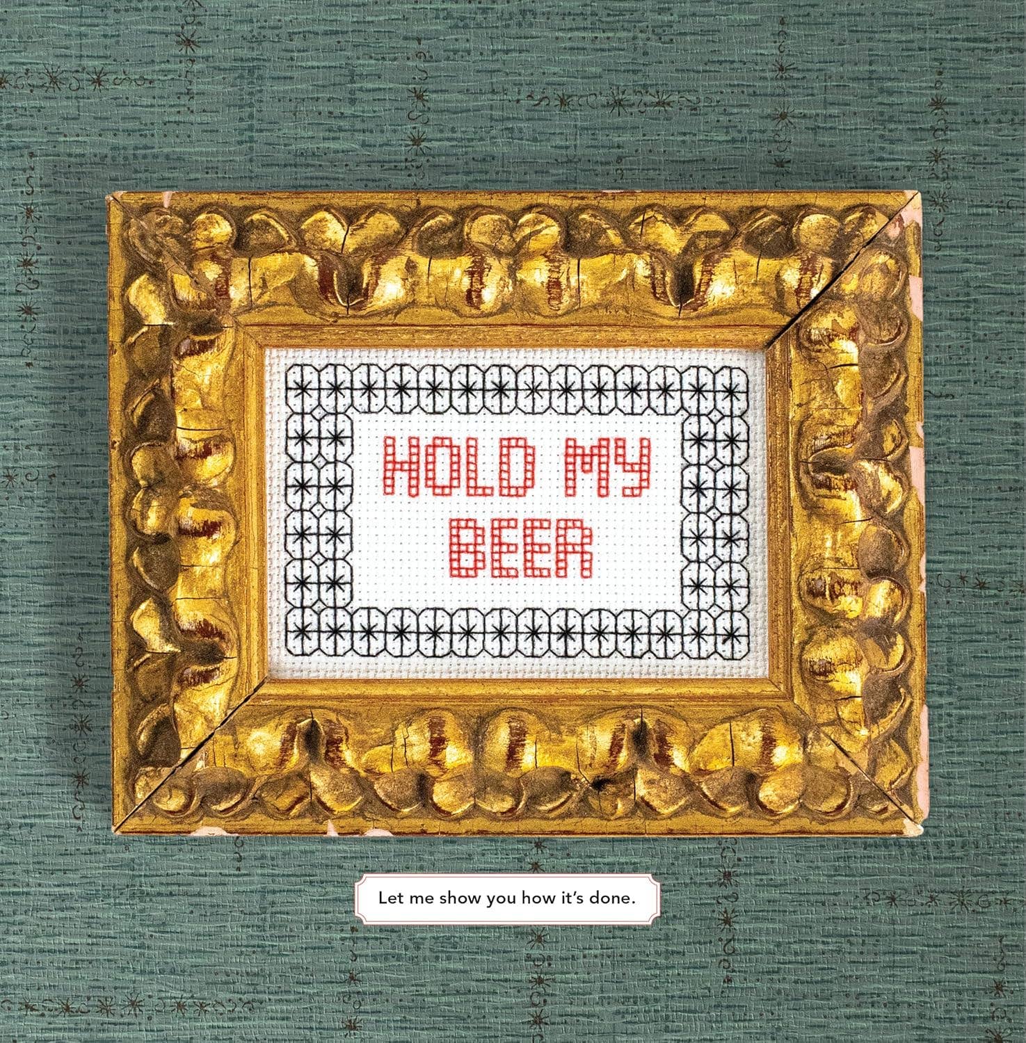 Gold-framed cross-stitched sign with 'Hold My Beer' text on a textured green background.