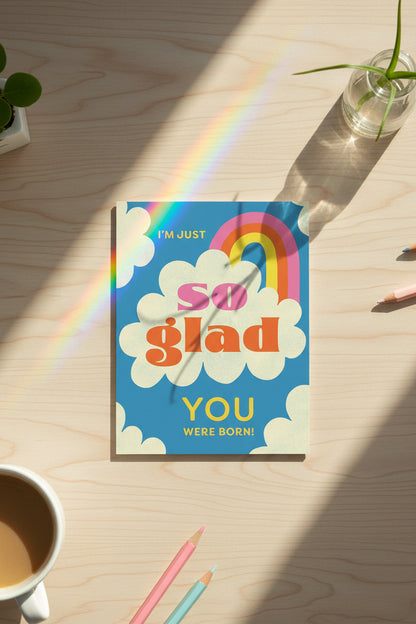 Card with rainbow, clouds, and text 'I'm just so glad you were born!' on a blue background