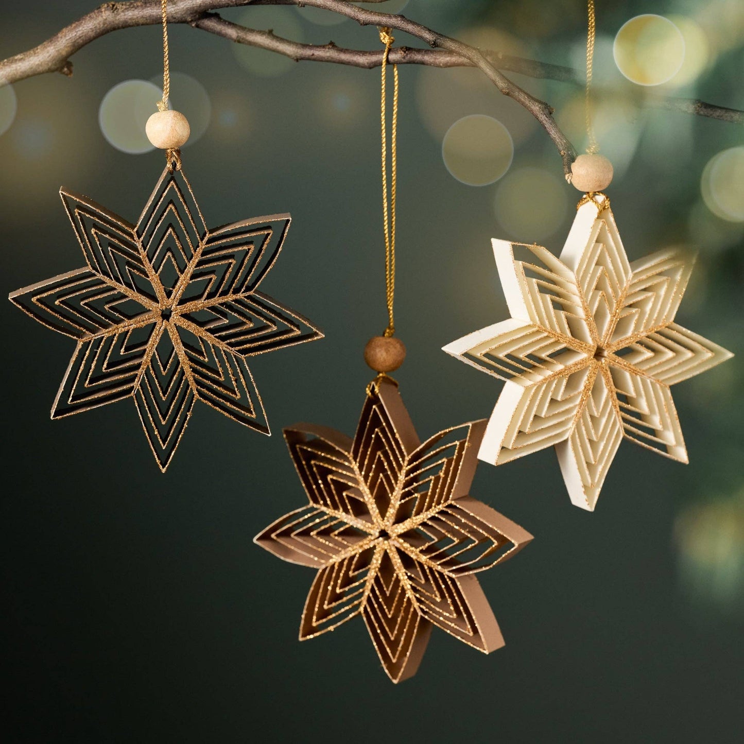 A view of three Nukeela Paper Star ornaments in three neutral holiday colors with a holiday background