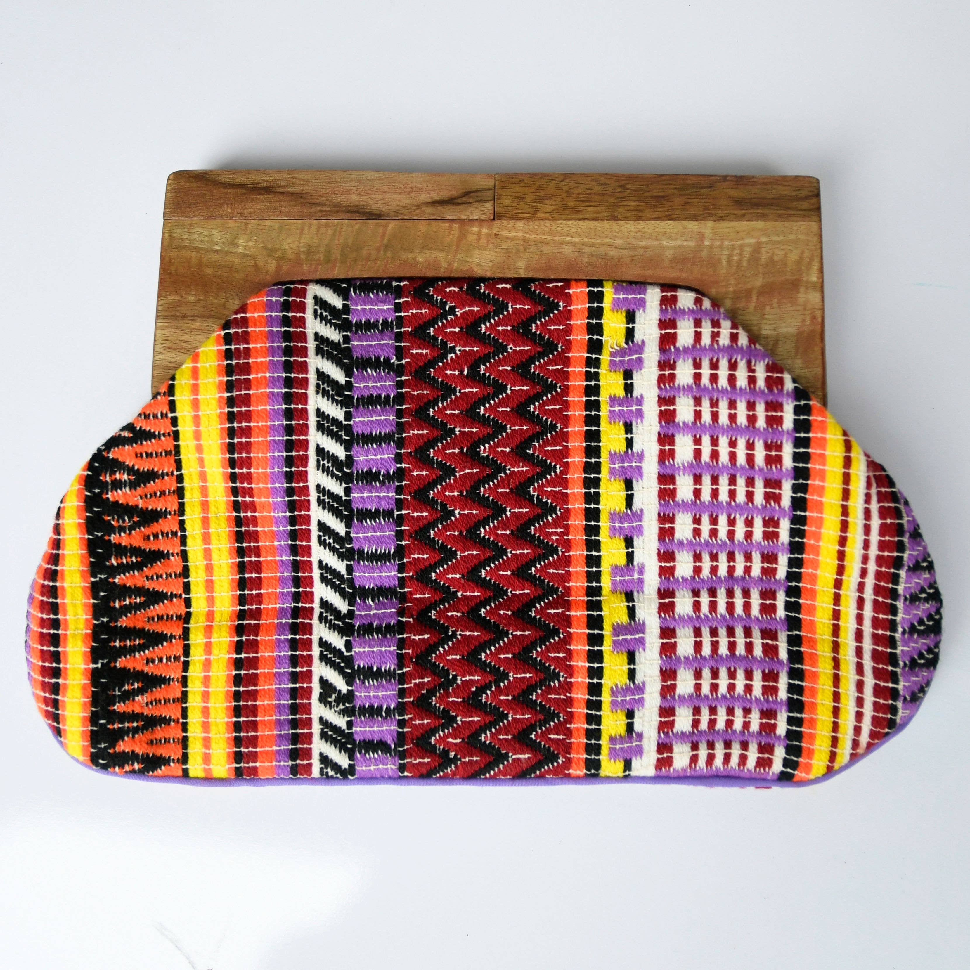 Colorful patterned clutch bag on a wooden block against a white background